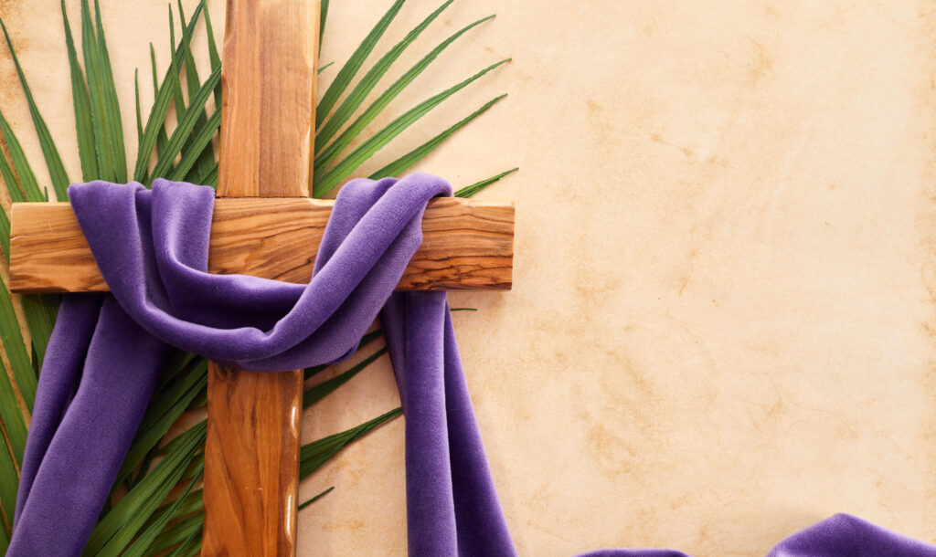 Imagen decorativa de una cruz de madera sobre una hoja de palma, con un lazo violeta